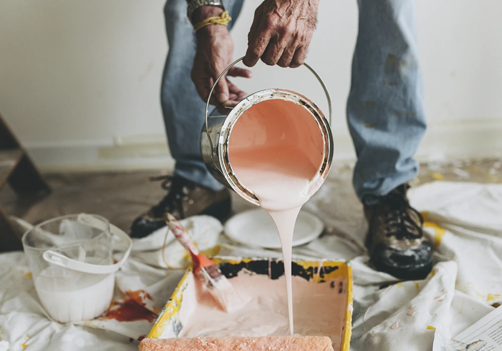 A man, pouring paint into a container to start painting